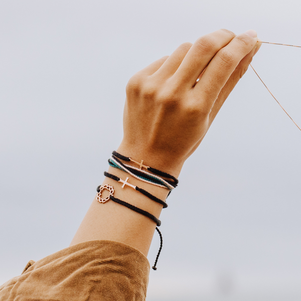 Rizen Jewelry Model wearing Made4Ministry Child Of God Cross Bracelet in Rose Gold Black macrame cord bracelet. Styled with Christian friendship bracelets. 