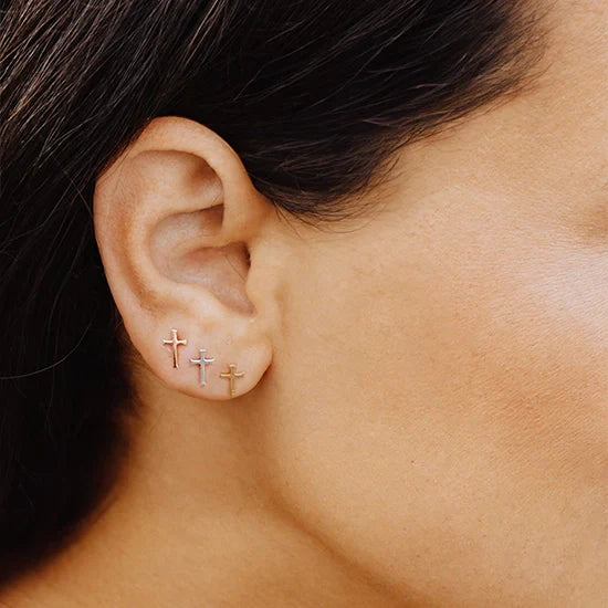 Close up of Christian woman wearing 3 pairs of the mini Cross Stud Earrings in sterling silver, rose, and yellow gold vermeil from the Calvary Collection by Rizen Jewelry.